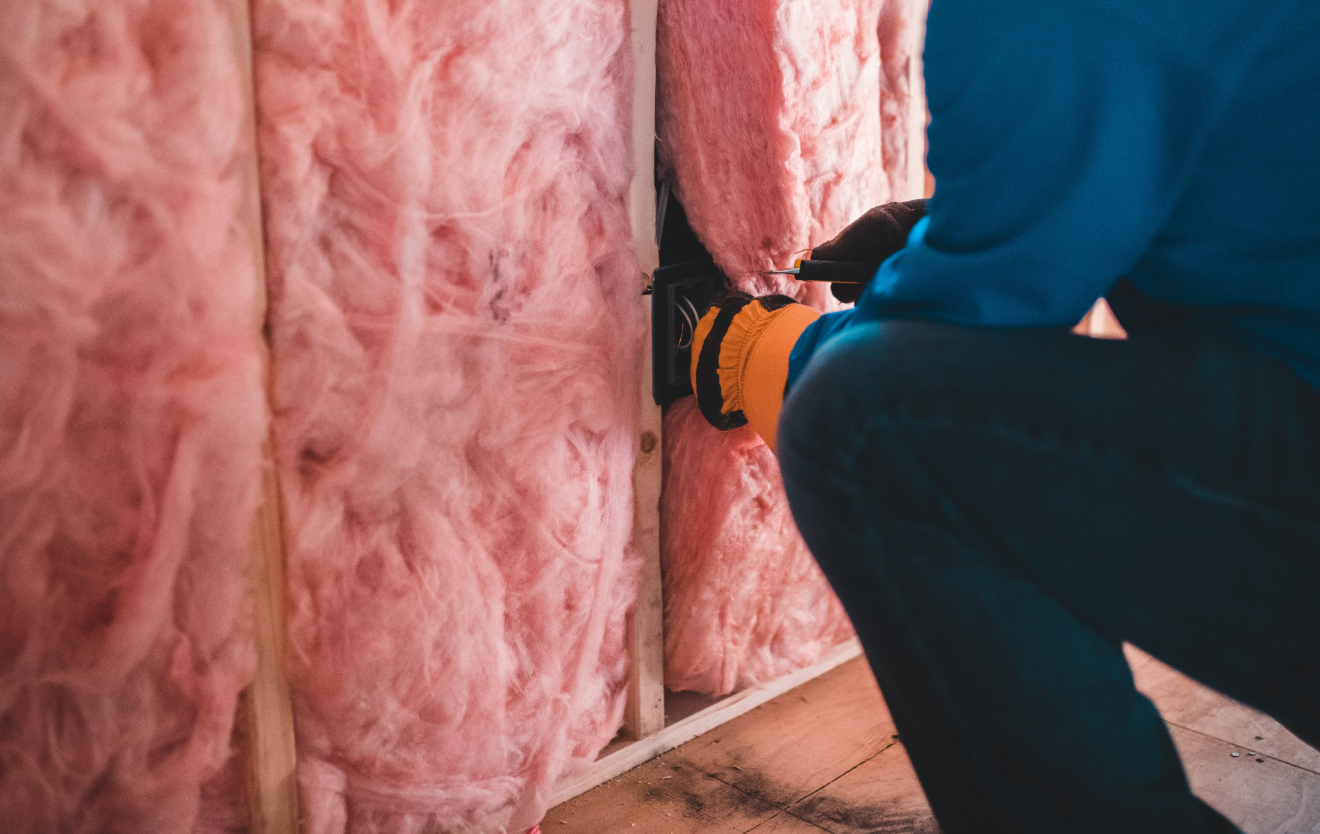 A man is working on a wall with pink insulation.
