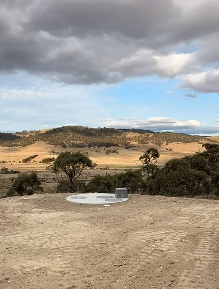 A flat, concrete pad with a small structure sits in a barren landscape, with hills and a cloudy sky in the background. — Demetrius Projects in Queanbeyan East, NSW