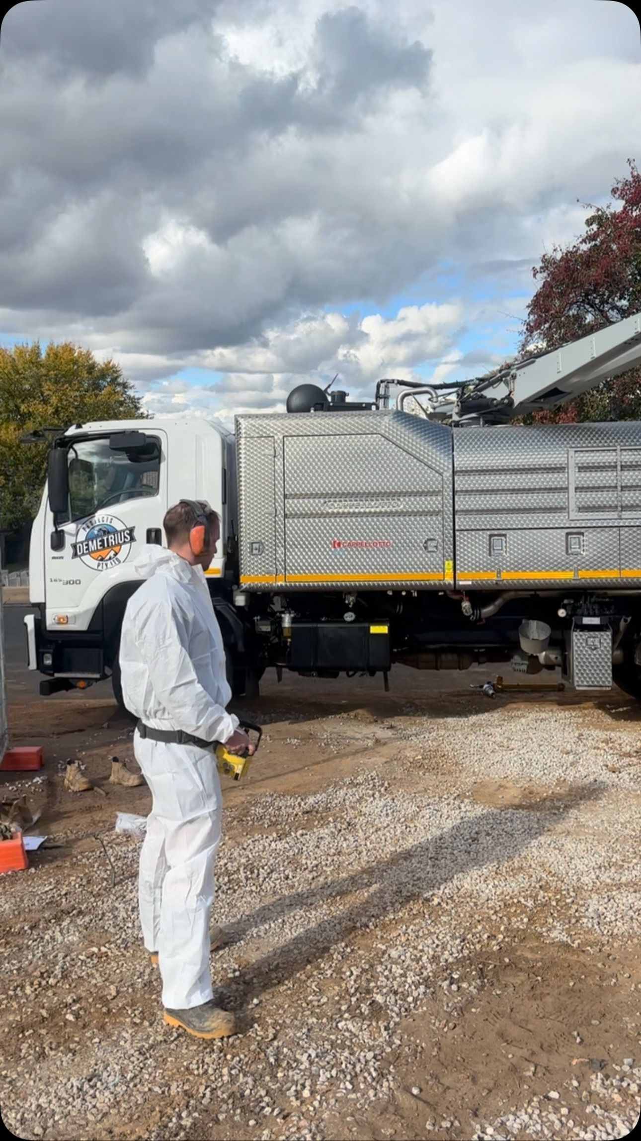 Man in white protective suit stands by a utility truck on a gravel driveway under a cloudy sky. — Demetrius Projects in Queanbeyan East, NSW