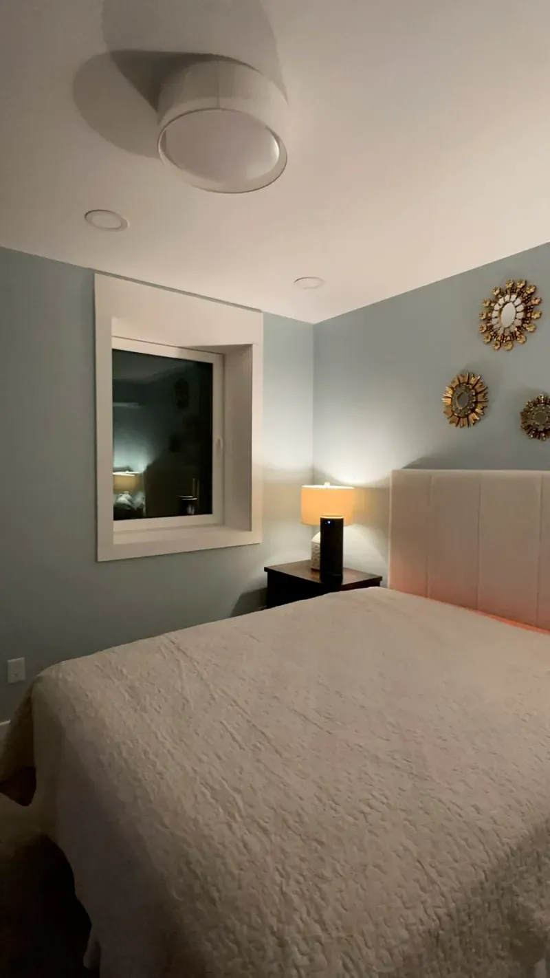 A bedroom with a bed , nightstand , lamp and window.