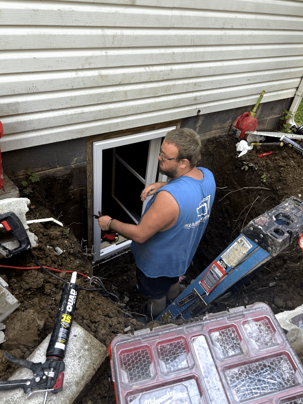 A man is working on a window in the basement of a house.
