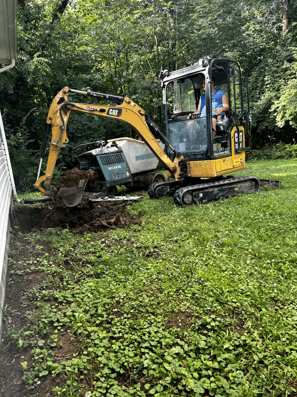 A man is driving a small excavator in a yard.