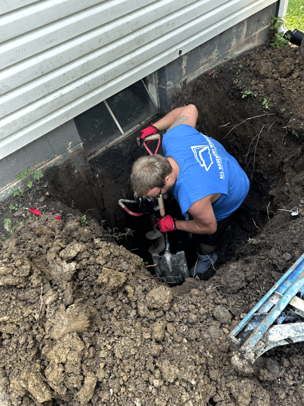 A man is digging a hole in the ground next to a house.