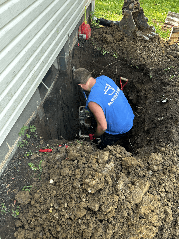 A man in a blue shirt is kneeling in the dirt next to a house.
