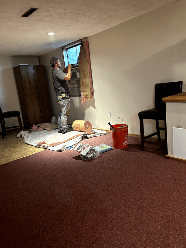 A man is working on a window in a basement.