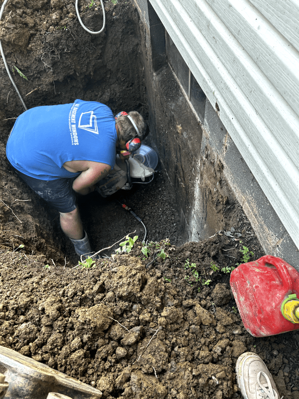 A man is digging a hole in the ground next to a building.