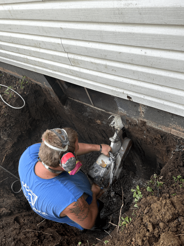 A man is cutting a hole in the ground next to a house.