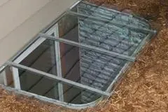 A window in the basement of a house with a glass roof.