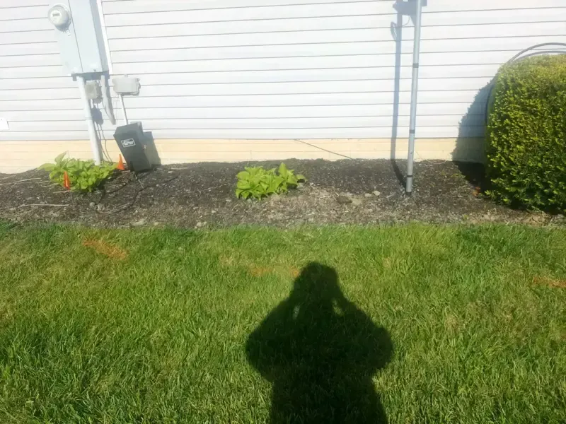 A person 's shadow is cast on the grass in front of a house.