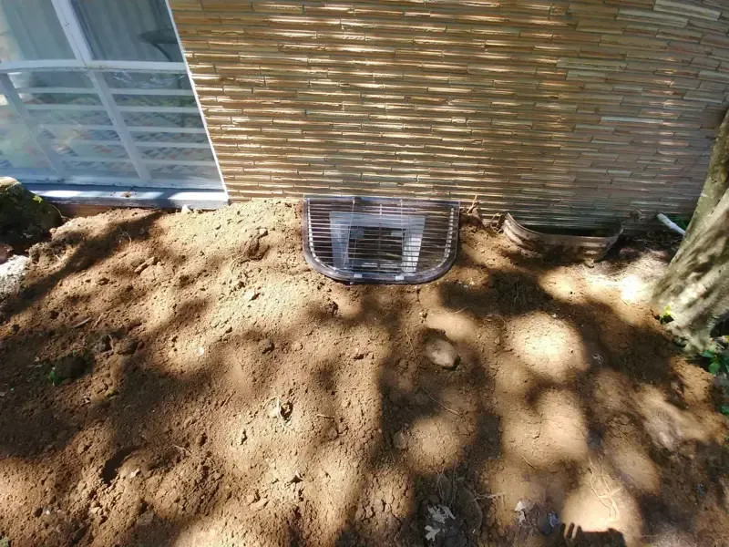 A window well is being installed on the side of a house.