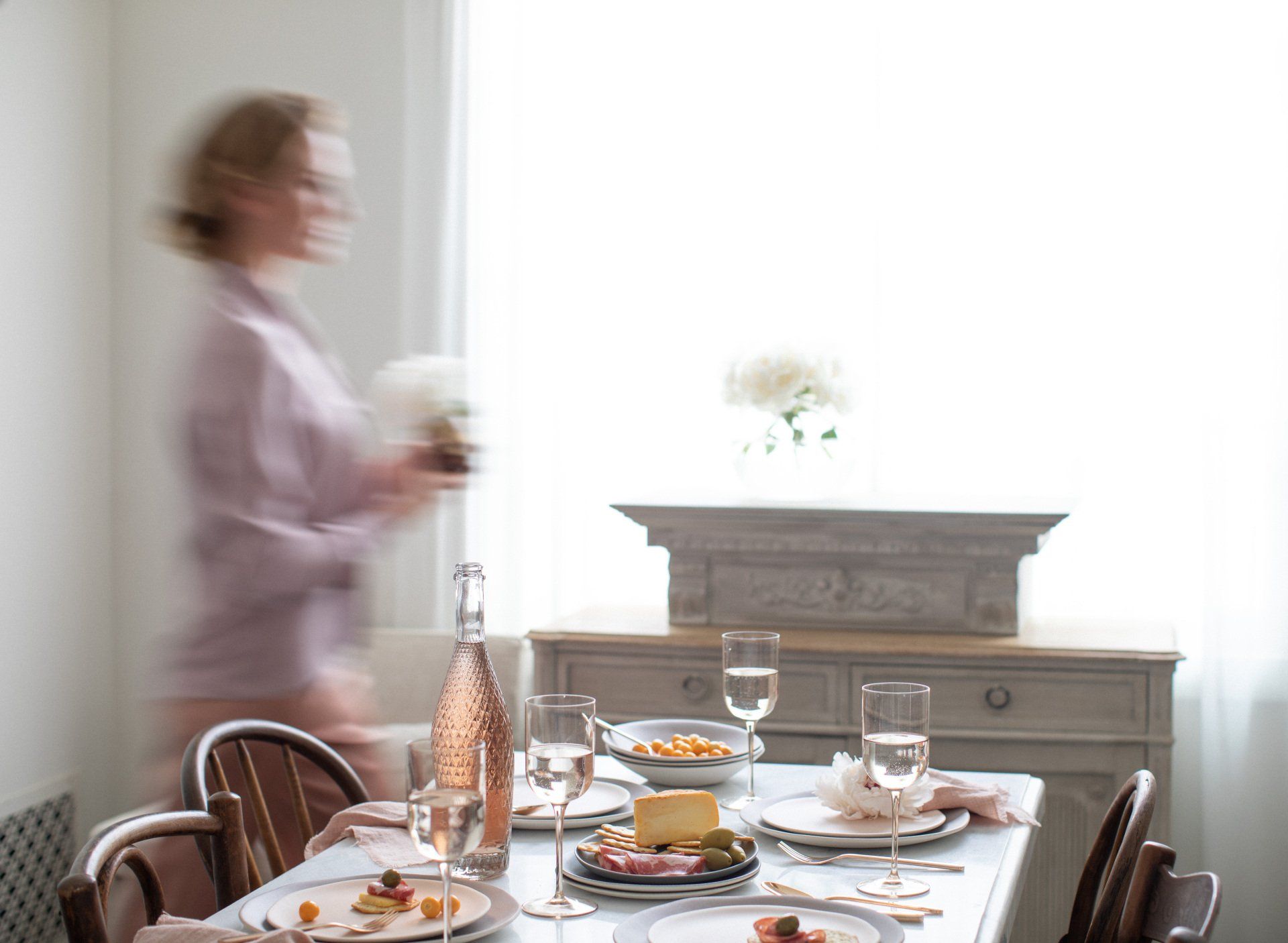 A blurry picture of a woman standing in front of a table set for a meal.