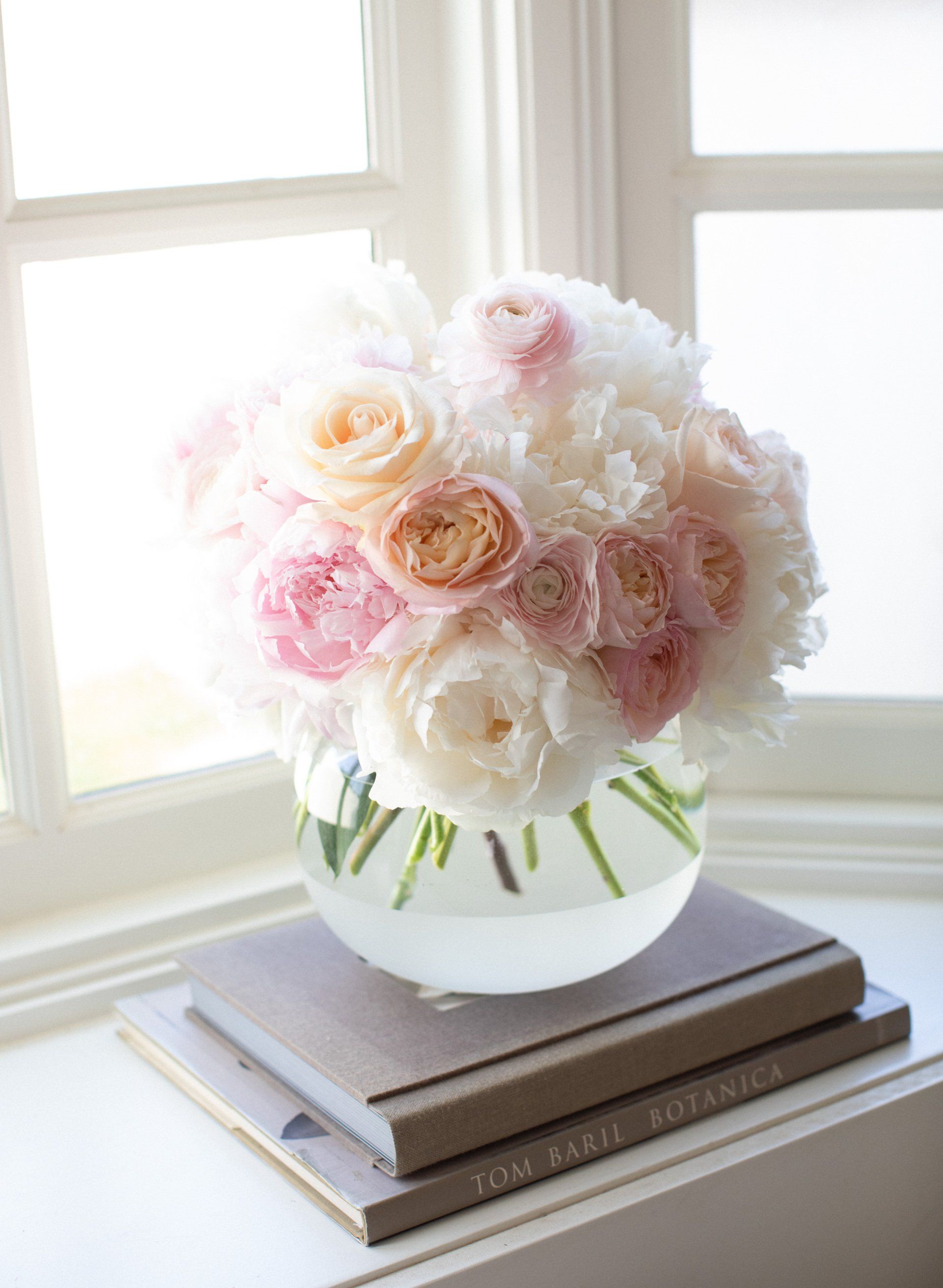 A vase filled with pink and white flowers is sitting on top of a stack of books.