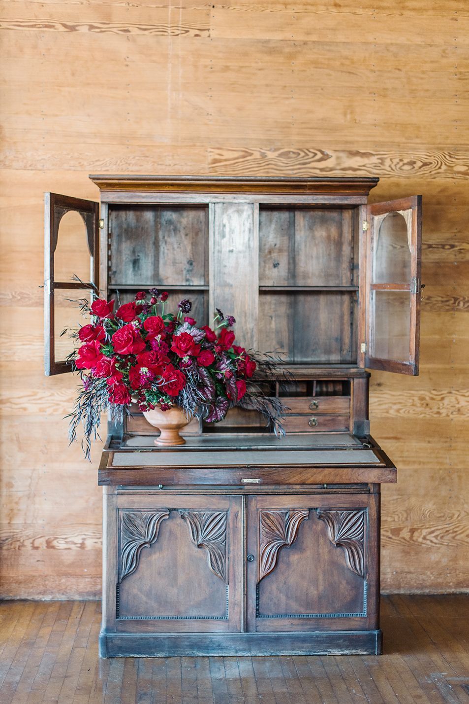 A wooden cabinet with a vase of red flowers on top of it.