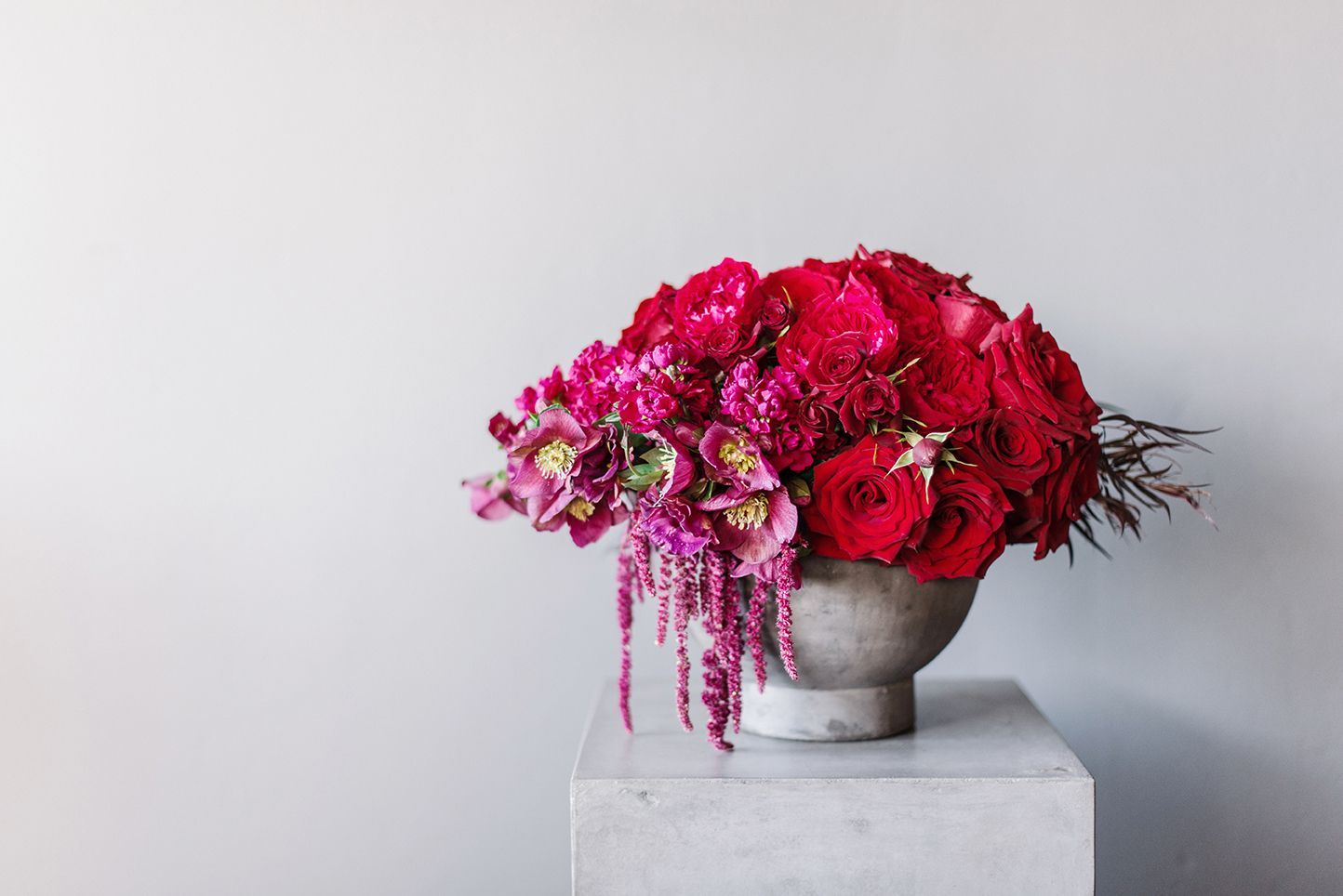 A vase filled with red roses and pink flowers is sitting on a marble block.