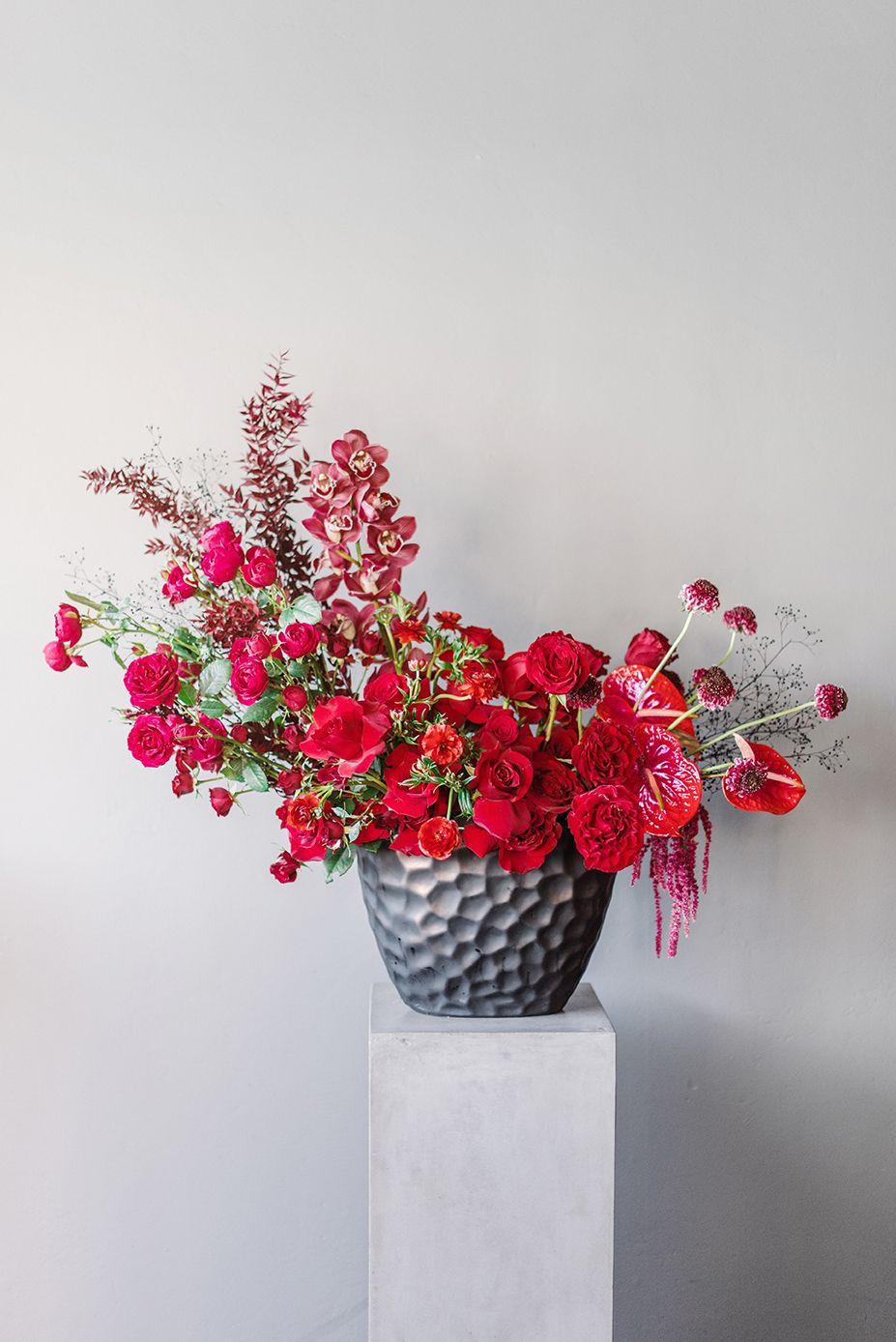 A vase filled with red flowers is sitting on a pedestal.