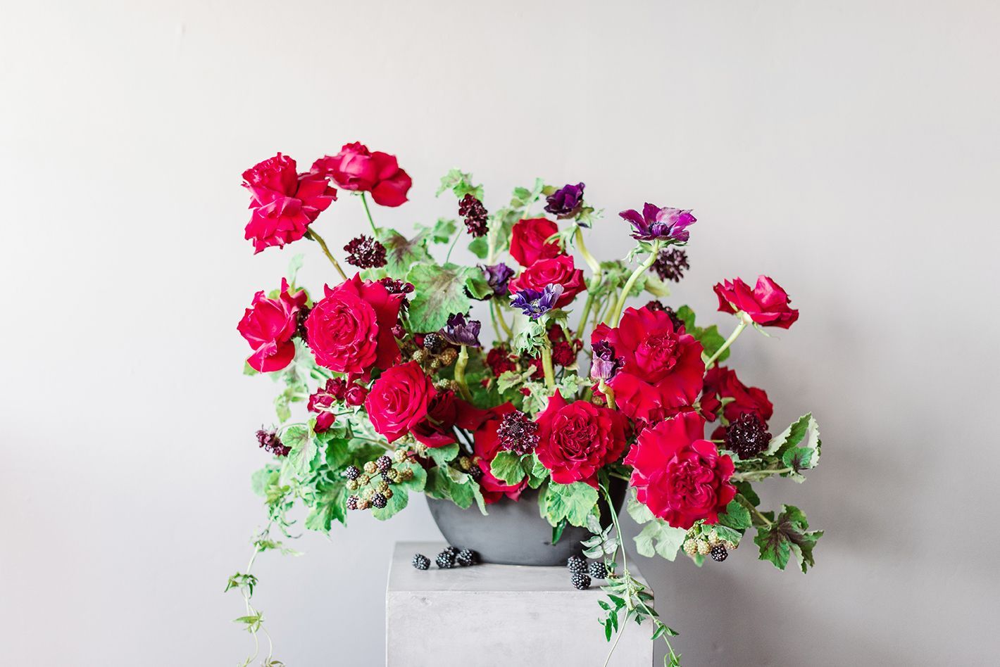 A vase filled with red roses and anemones is sitting on a concrete block.