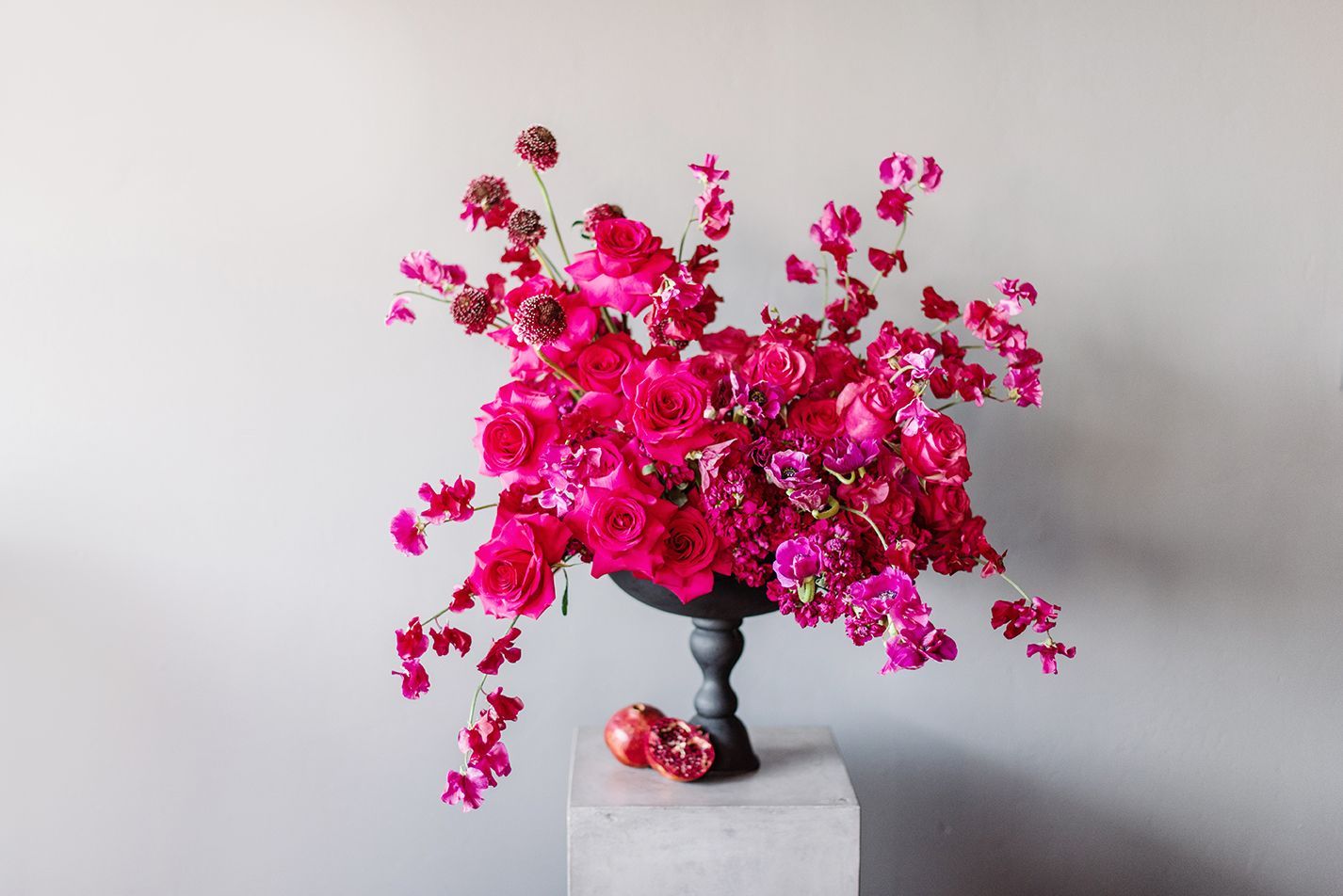 A vase filled with pink flowers and pomegranates on a pedestal.