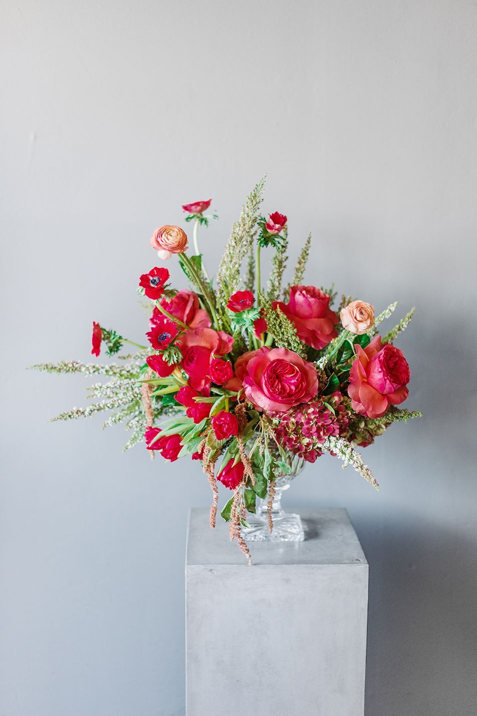 A vase filled with red flowers is sitting on top of a concrete pedestal.