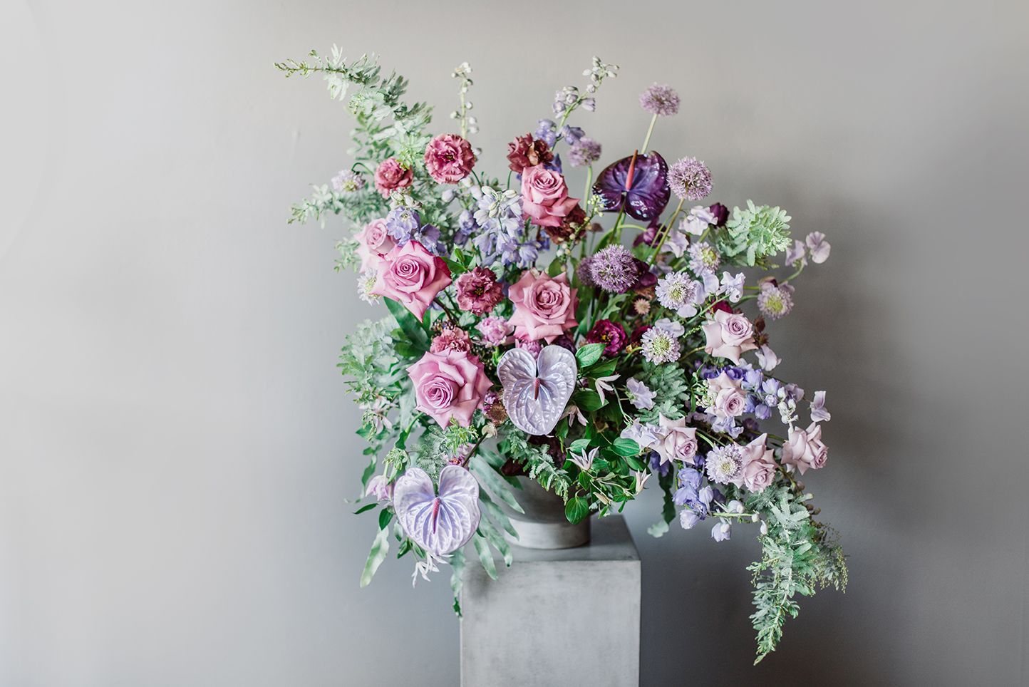 A vase filled with purple and pink flowers is sitting on a concrete pedestal.