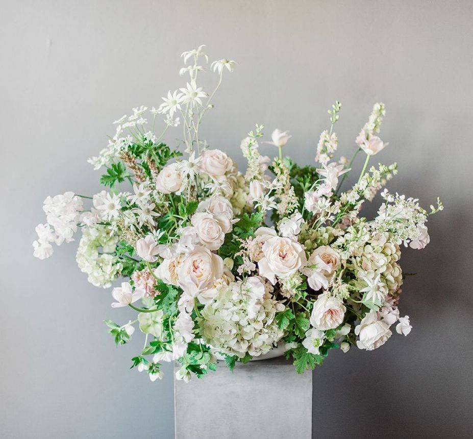 A vase filled with white flowers is sitting on top of a concrete pedestal.