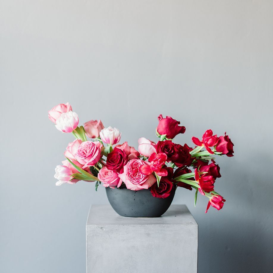 A vase filled with pink and red flowers is sitting on a concrete block.