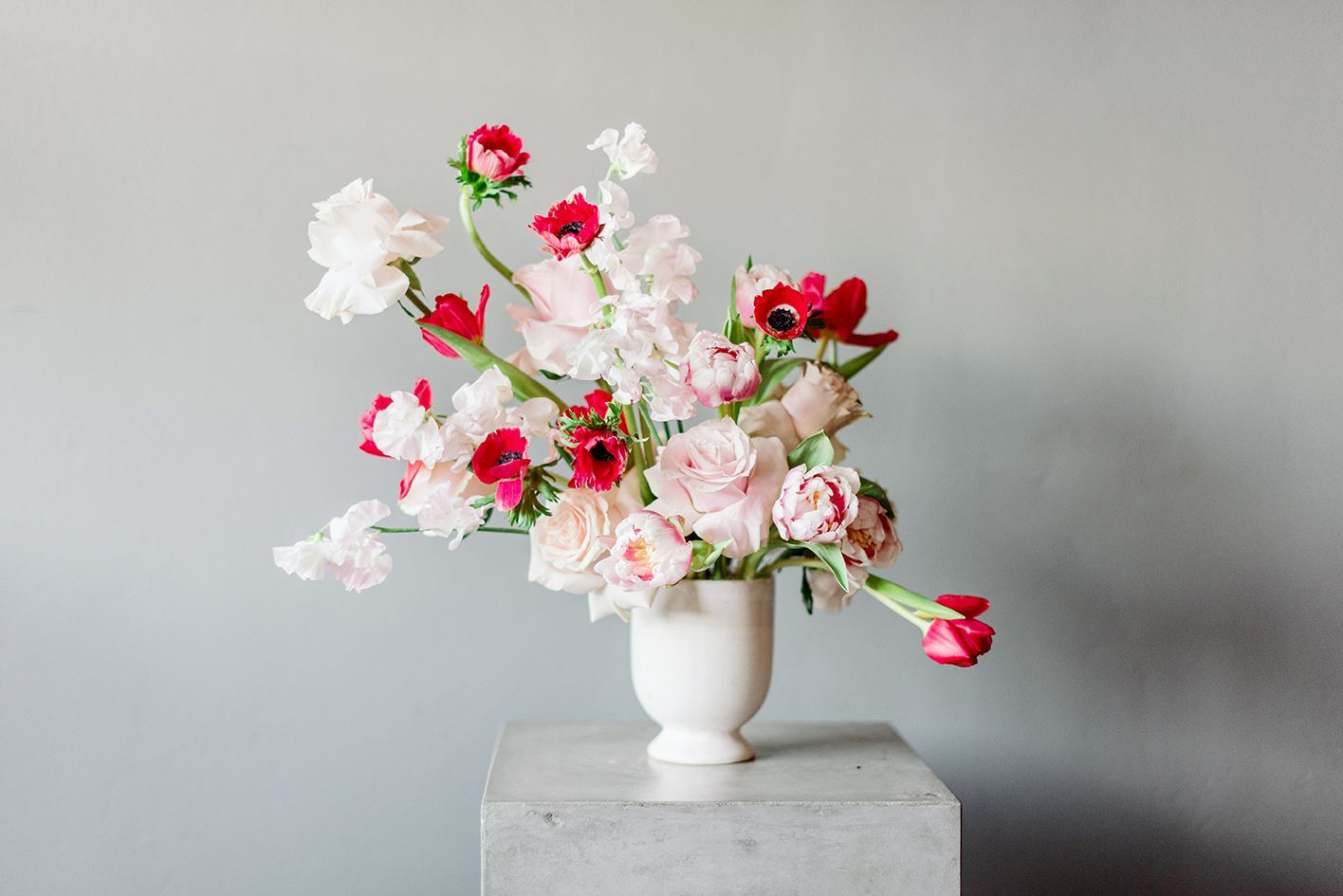 A vase filled with pink and white flowers is sitting on a marble pedestal.