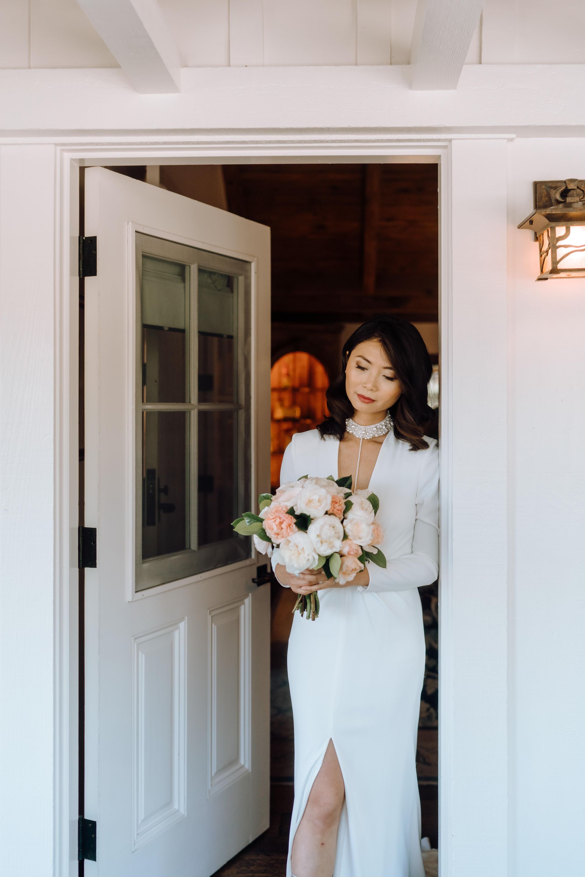 A woman in a white dress is standing in a doorway holding a bouquet of flowers.