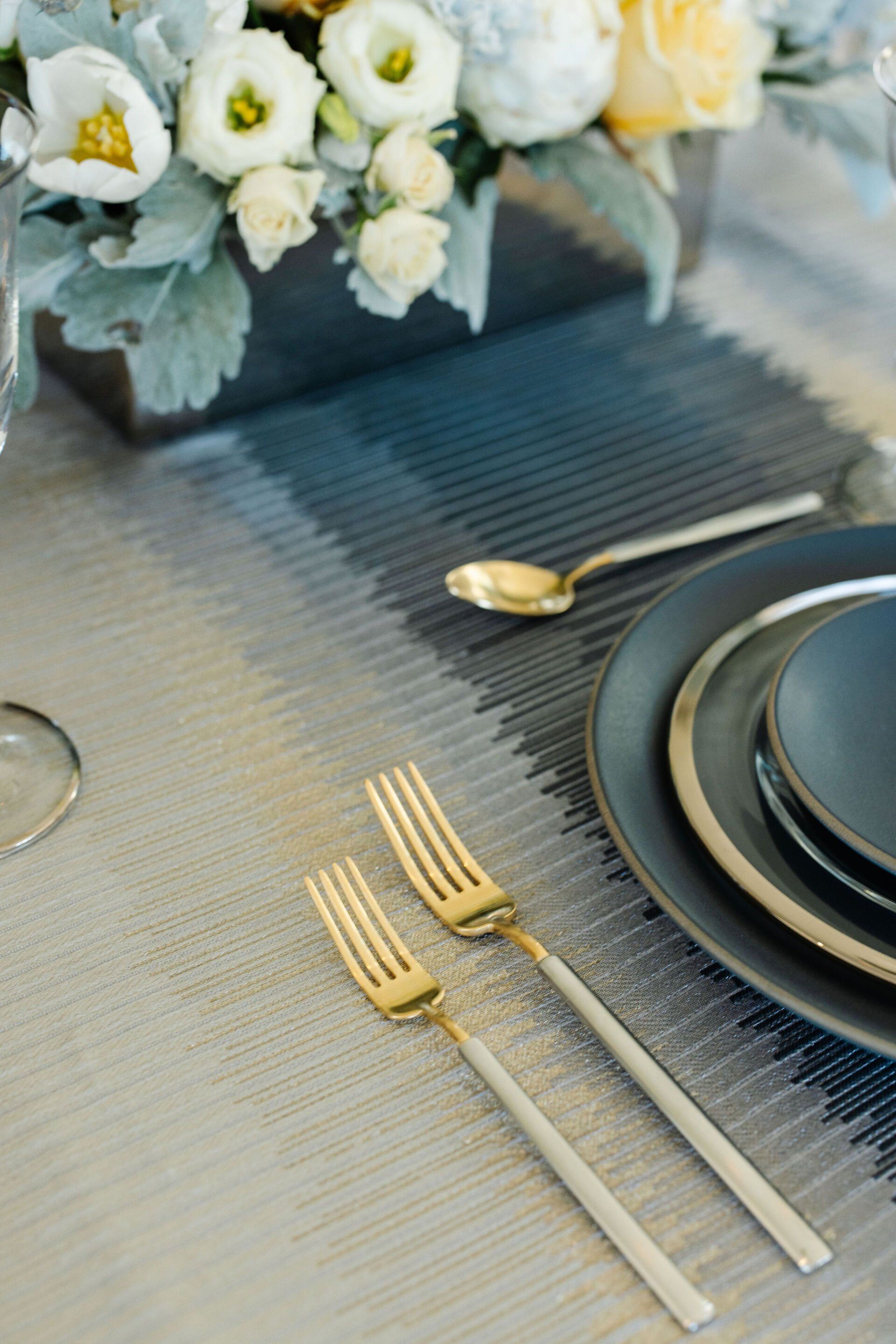 A table setting with plates , forks , spoons and a vase of flowers.