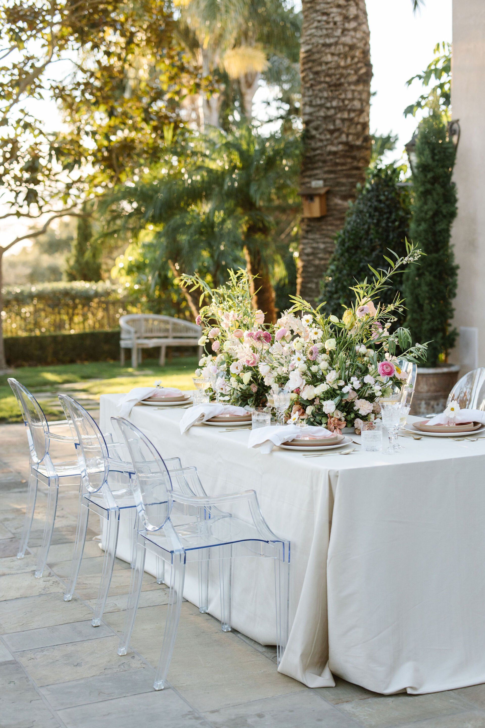 A long table with clear chairs and flowers on it.