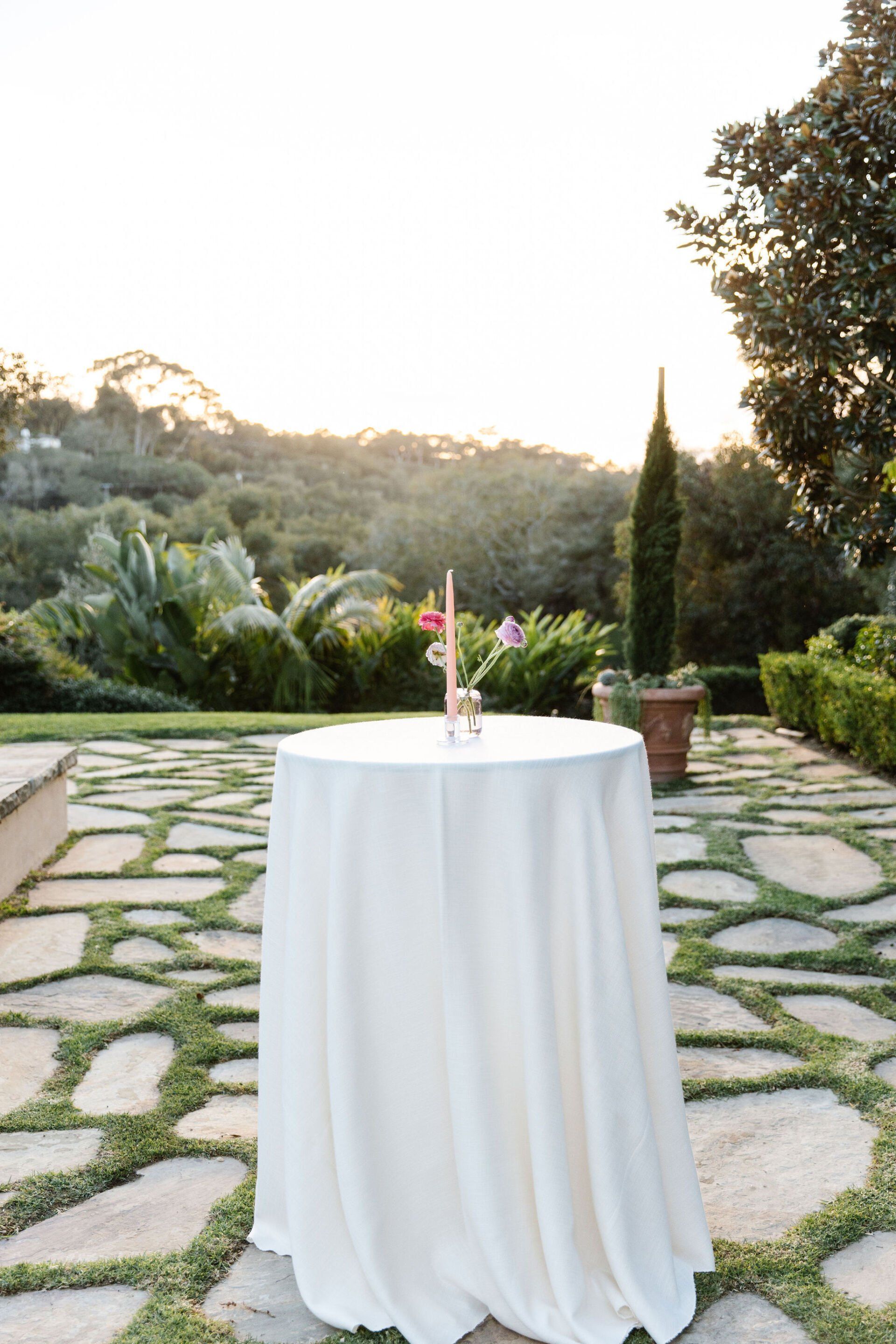 A white table with a white tablecloth is sitting on a stone patio.