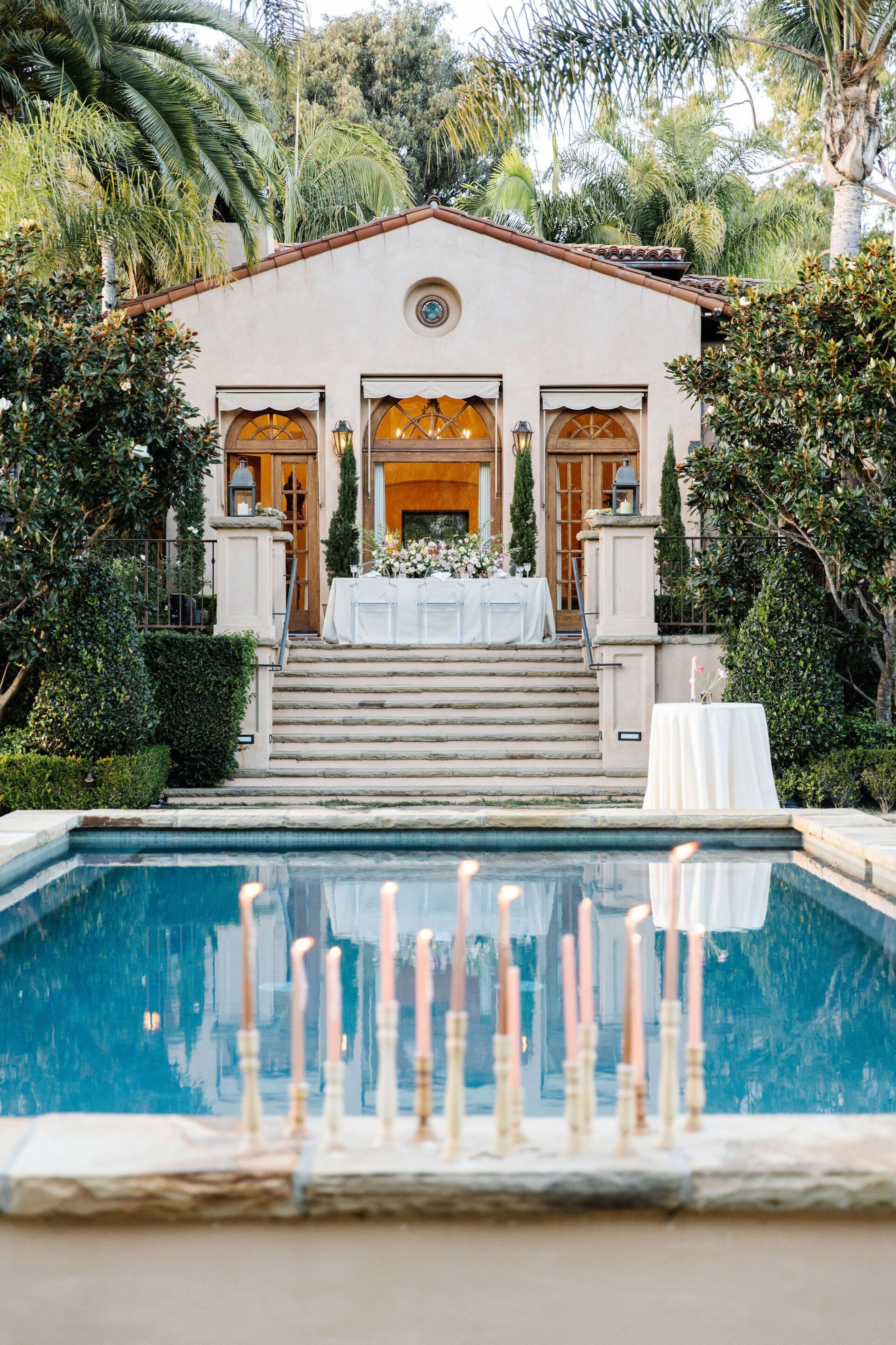 A row of candles are sitting on the edge of a swimming pool in front of a building.