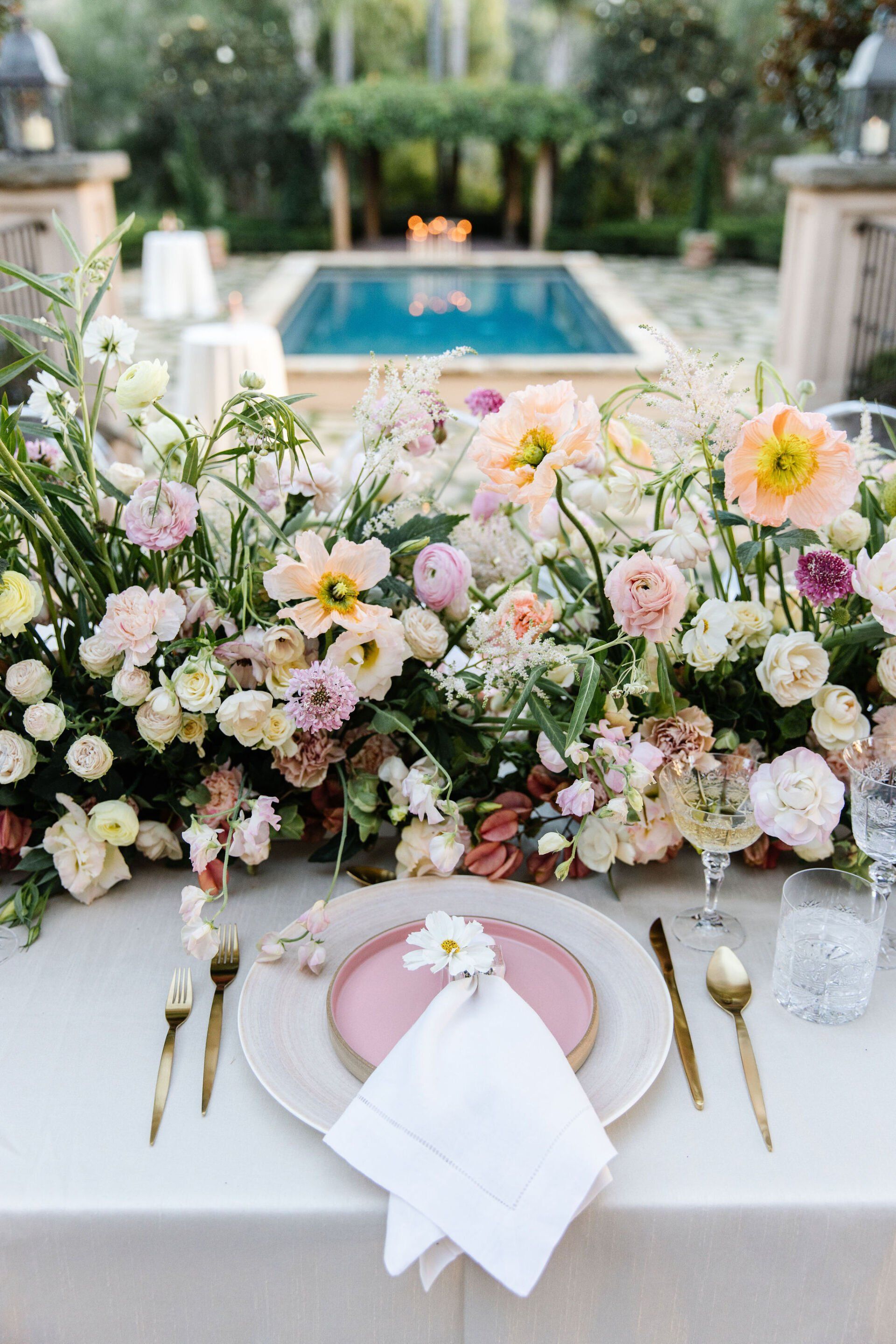 A table with plates , silverware , and flowers on it in front of a pool.