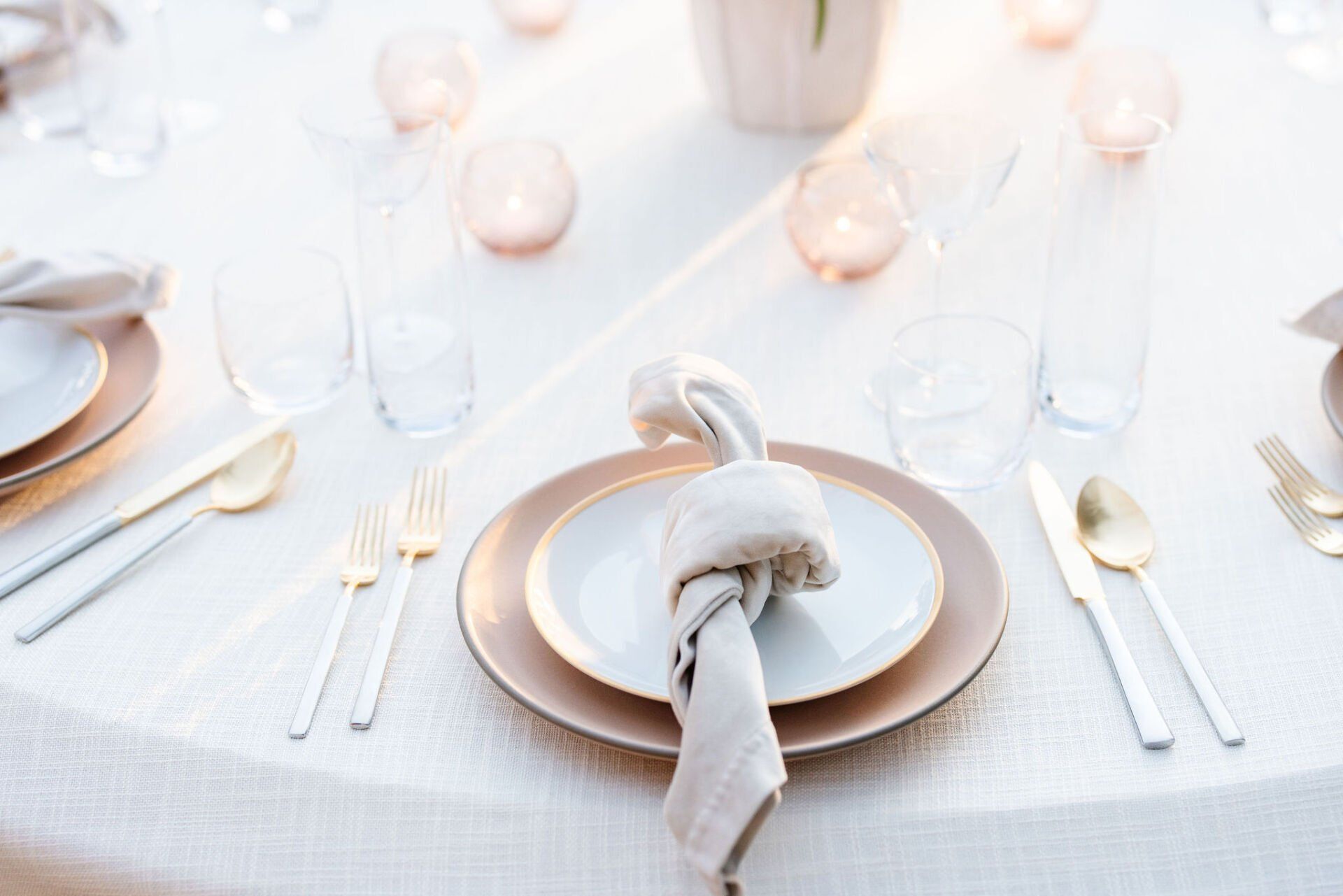A table set for a wedding reception with plates , silverware , and candles.