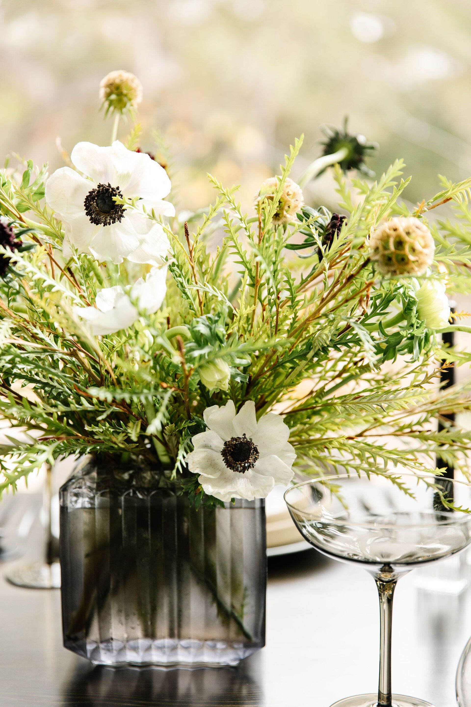 A vase filled with flowers is sitting on a table next to a wine glass.