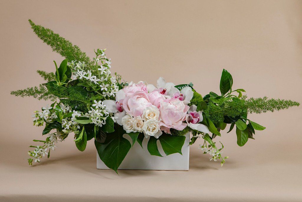 A white vase filled with pink and white flowers and greenery on a table.