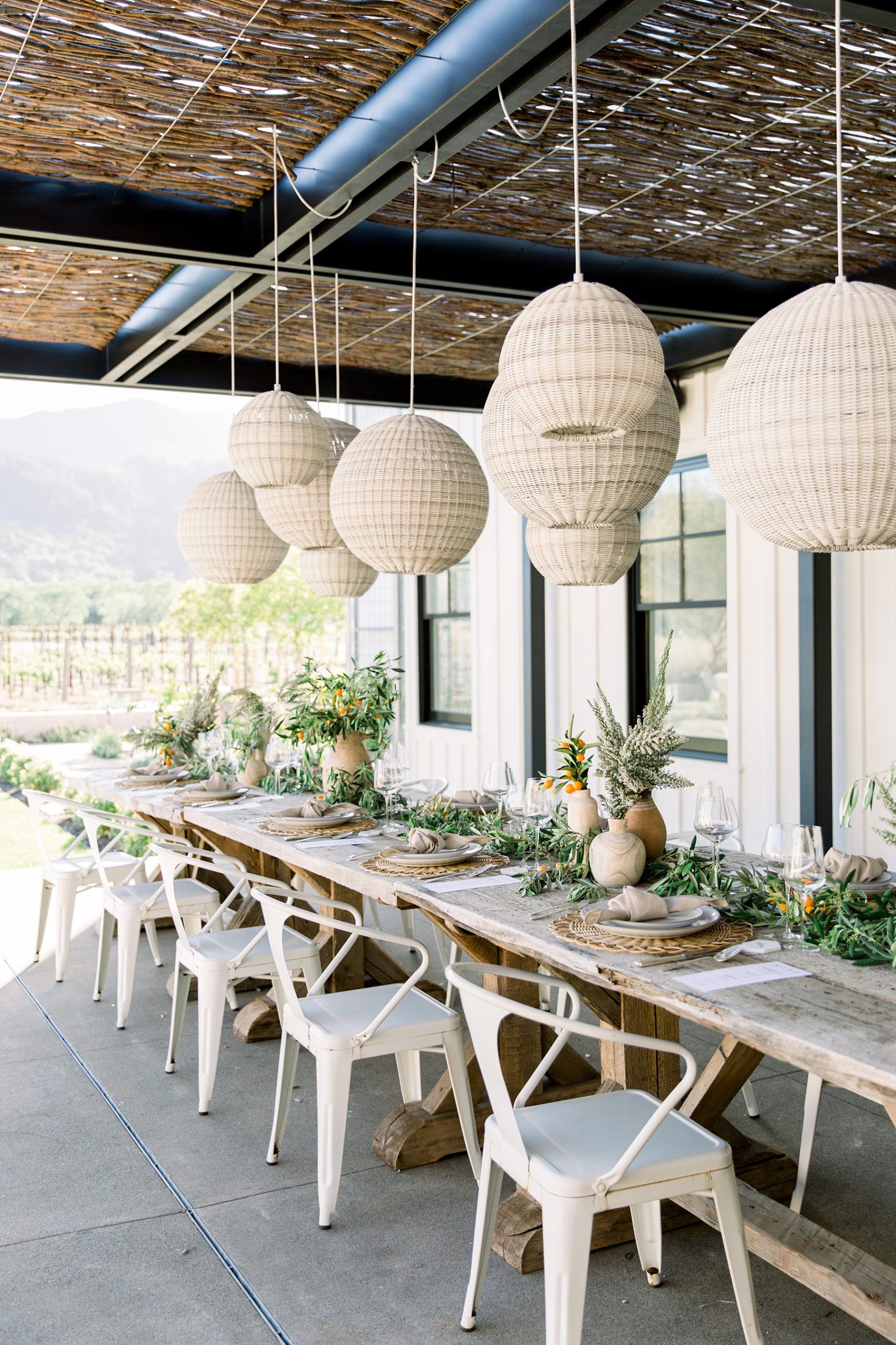 A long wooden table with white chairs under a canopy.