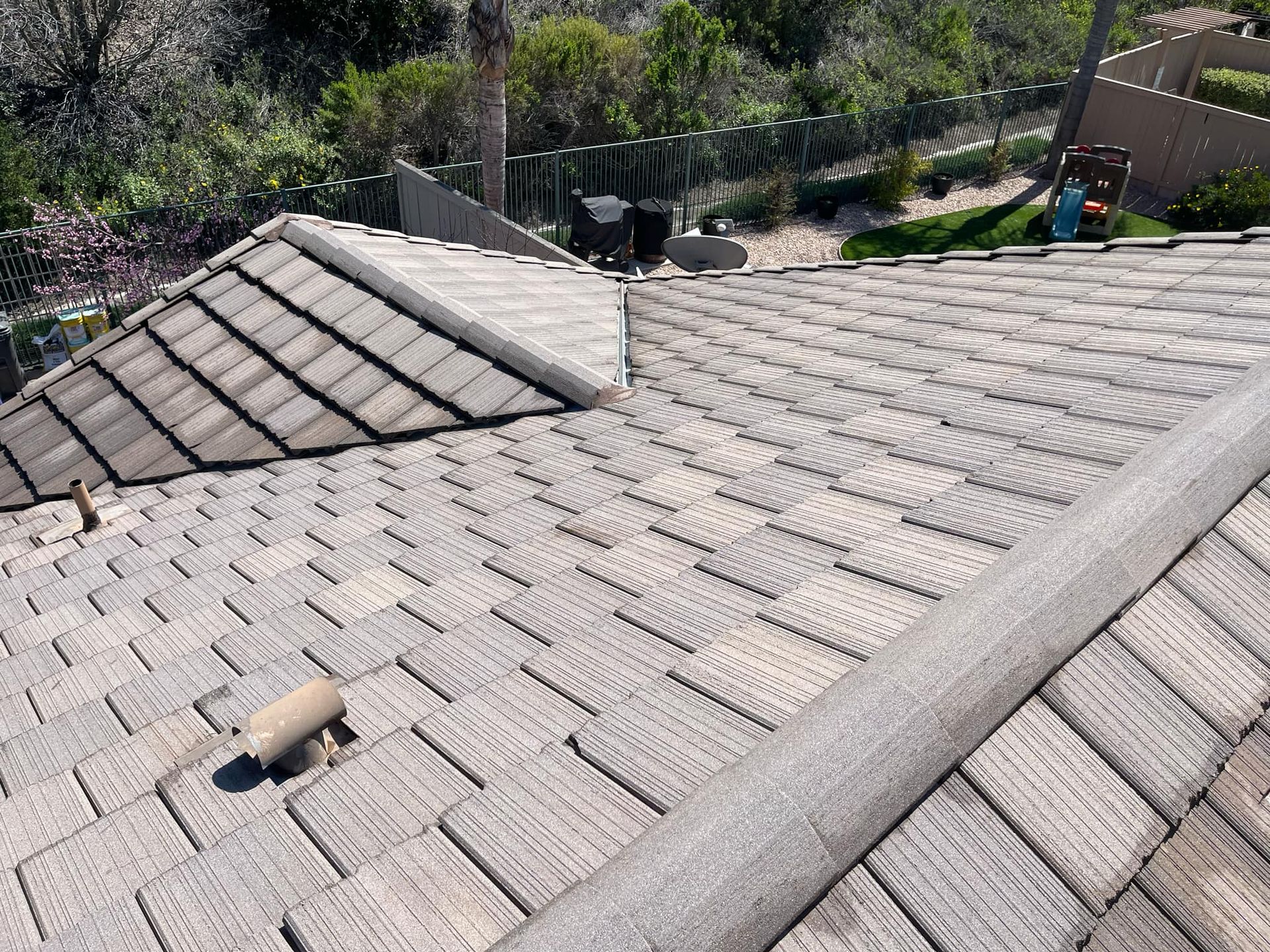 Roof with gray shingles and a ridge vent, viewed from above near a yard with trees and a fence