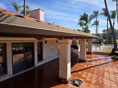 Sunny patio with terracotta tiles, white columns, and palm trees beside a waterfront home