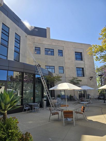 Courtyard patio with tables and umbrellas beside a modern stone building under a clear blue sky