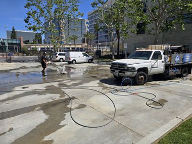 Flooded urban street with two white work trucks, hoses on the ground, and a worker near wet pavement