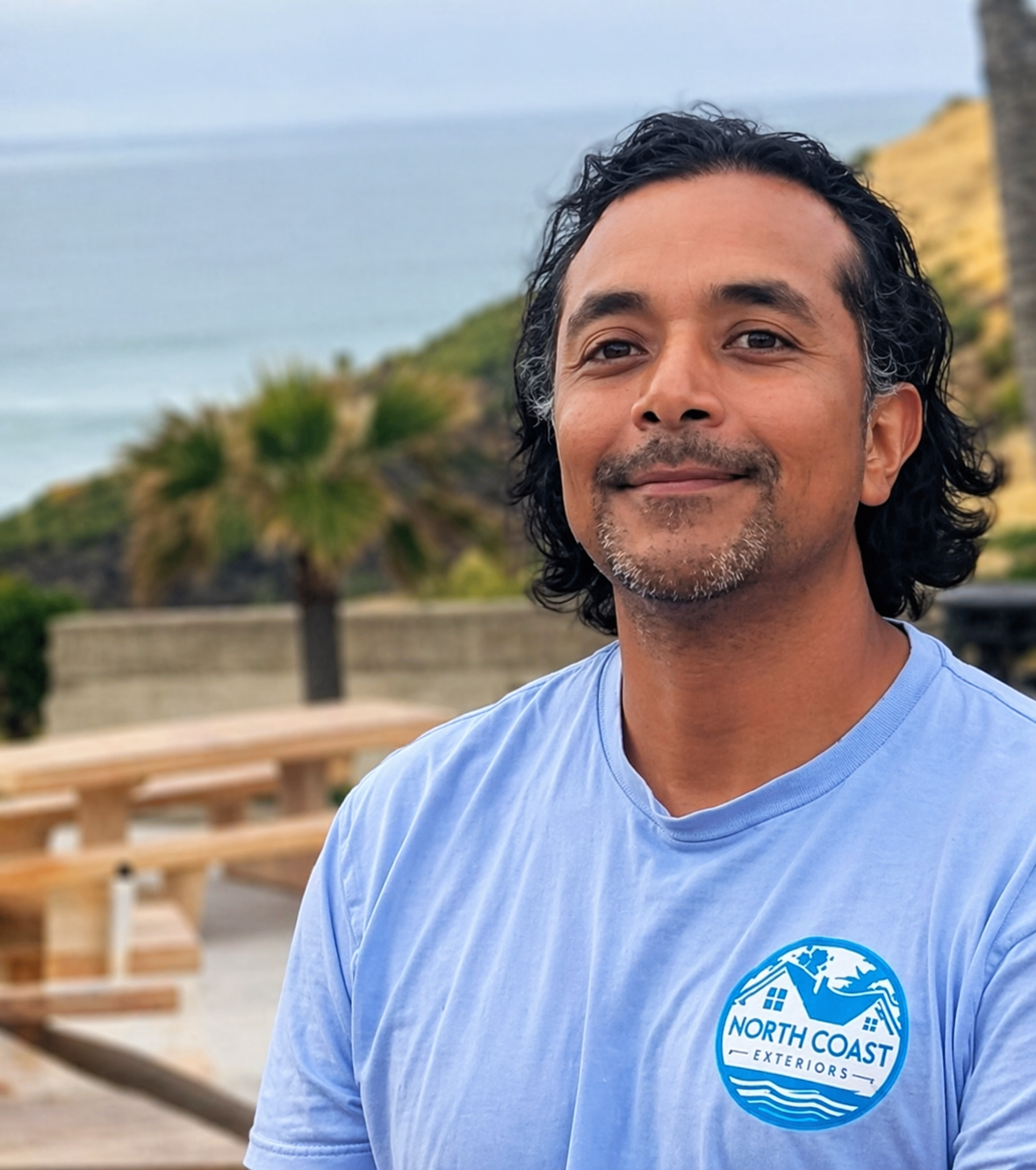 Smiling person in a light blue shirt at a seaside picnic area with ocean in the background