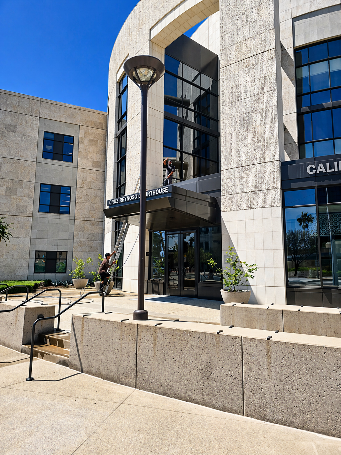 Modern stone building entrance with glass doors, lamppost, steps, and a person standing outside