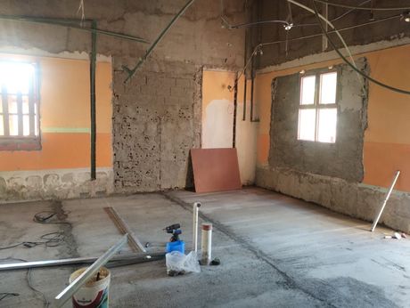 Habitación sin terminar con suelo de hormigón, paredes a la vista, ventanas y materiales de construcción.