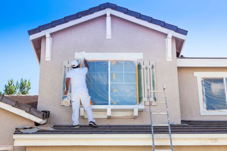 Obrero pintando la pared exterior de una casa en un andamio en la azotea.