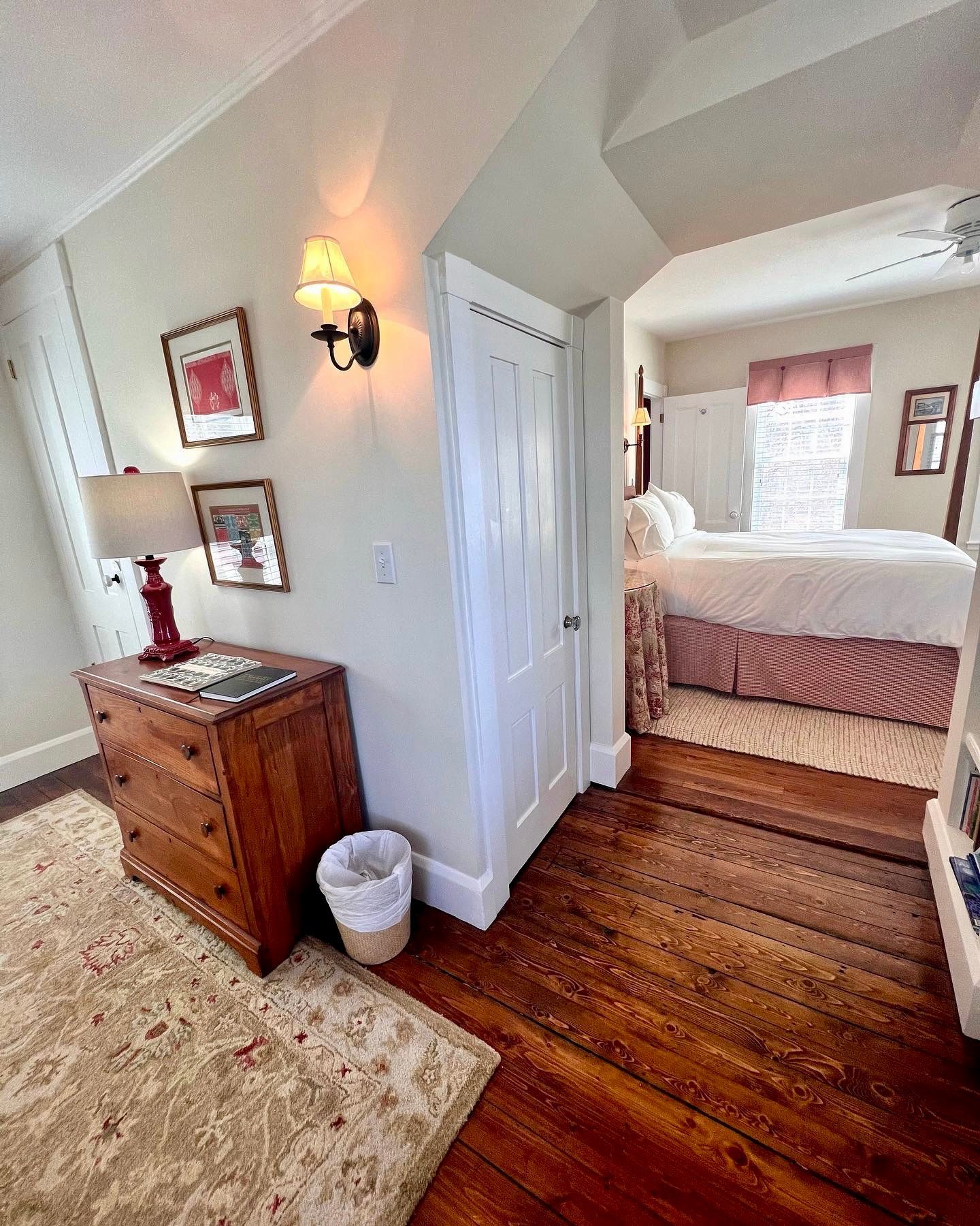 A bedroom with a bed , dresser , lamp and trash can.