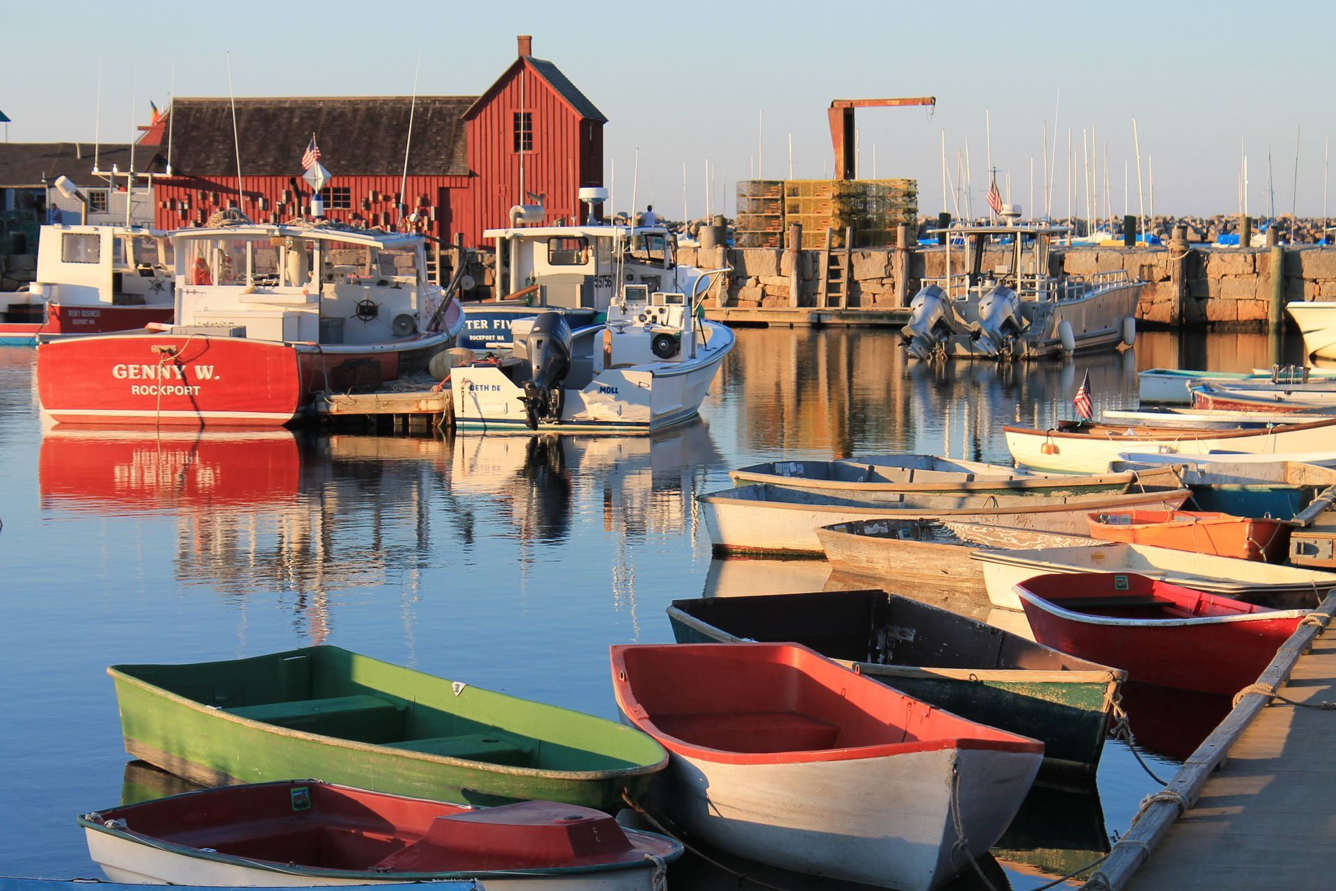 A row of boats are docked in a harbor with a red building in the background