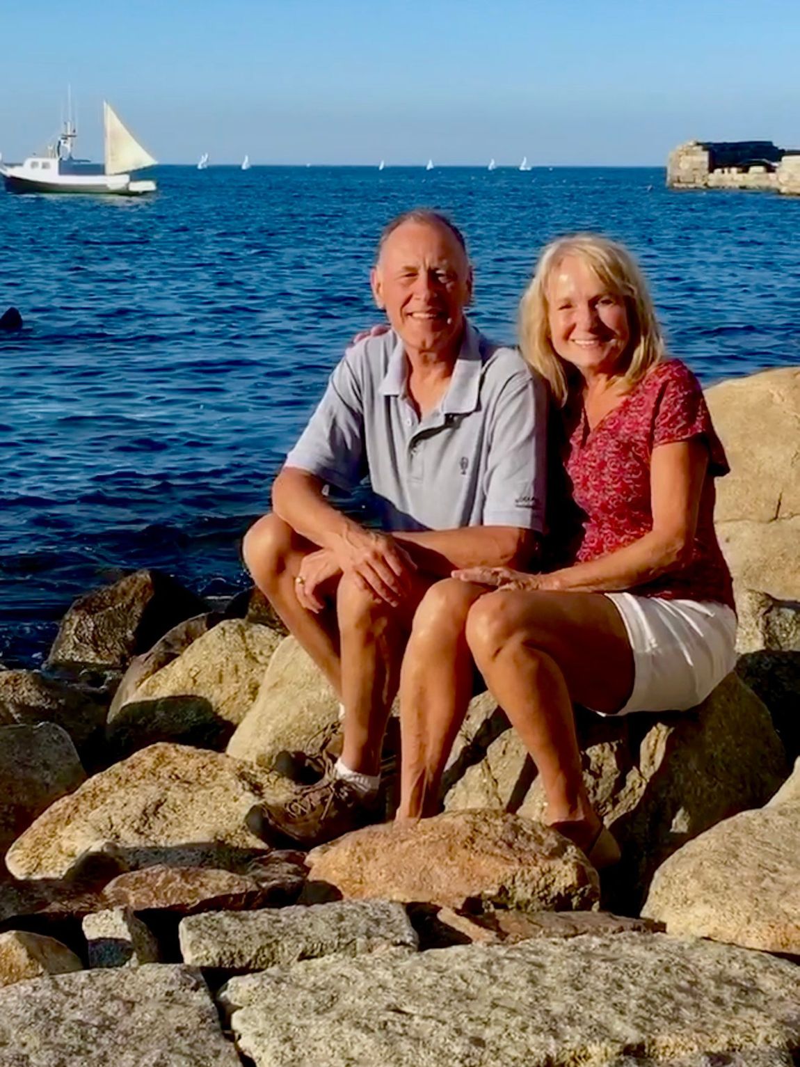 A man and a woman are sitting on rocks near the ocean.