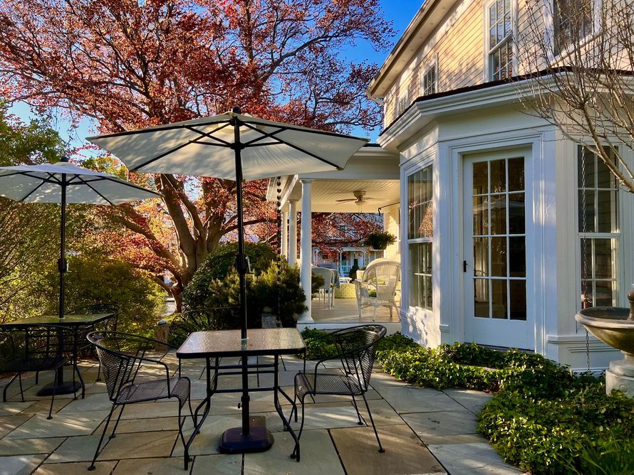 A patio with tables and chairs and umbrellas in front of a white house.
