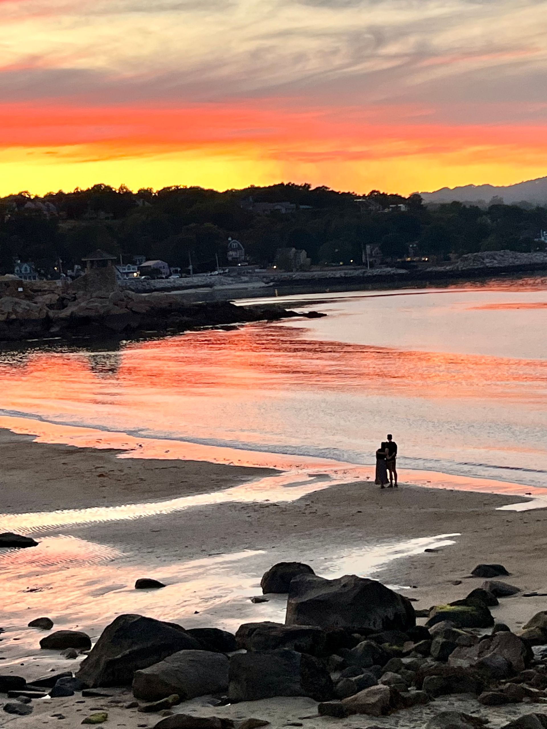 A couple standing on a beach at sunset.