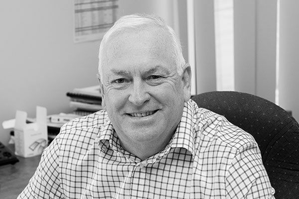 A smiling professional sits in an office wearing a checkered button-down shirt.